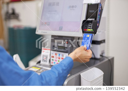 A senior woman pays with a card at a supermarket's self-checkout counter. A senior woman pays with a card at a supermarket's self-checkout counter. 139552342