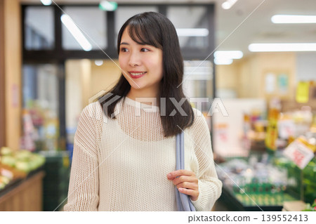 A young woman shopping at a supermarket while looking at her smartphone. A young woman shopping at a supermarket while looking at her smartphone. 139552413