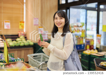 A young woman shopping at a supermarket while looking at her smartphone. A young woman shopping at a supermarket while looking at her smartphone. 139552416