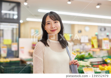 A young woman shopping at a supermarket while looking at her smartphone. A young woman shopping at a supermarket while looking at her smartphone. 139552479