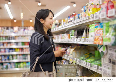 A businesswoman shopping at a supermarket while looking at notes on her smartphone. A businesswoman shopping at a supermarket while looking at notes on her smartphone. 139552668