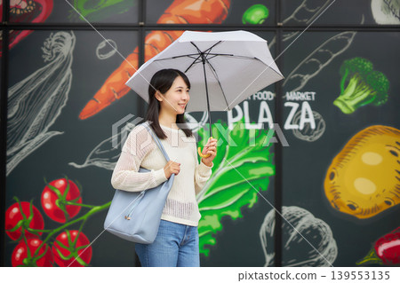 一位年輕女子撐著陽傘去超市。 一位年輕女子撐著陽傘去超市。 139553135