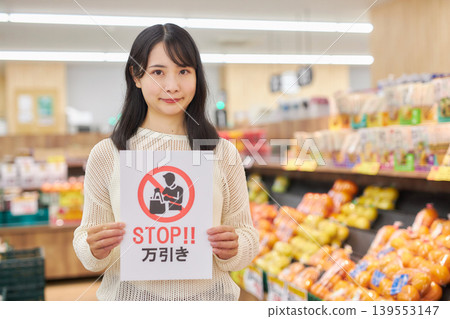 A young woman holding an anti-shoplifting sign in front of products in a supermarket. A young woman holding an anti-shoplifting sign in front of products in a supermarket. 139553147