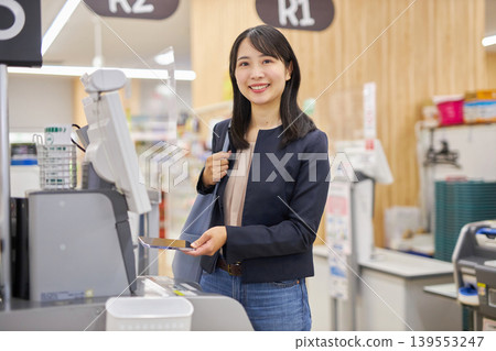 一位年輕女子正在使用智慧型手機在自助結帳櫃檯付款。 一位年輕女子正在使用智慧型手機在自助結帳櫃檯付款。 139553247