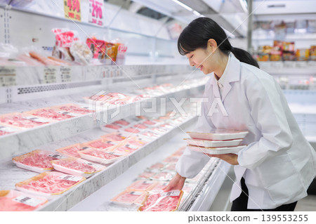 一位身穿白大褂的年輕女子正在超市整理肉類。 一位身穿白大褂的年輕女子正在超市整理肉類。 139553255