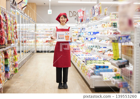 一位年輕女子在超市商品前舉著一塊關於食物浪費的標語牌。 139553260