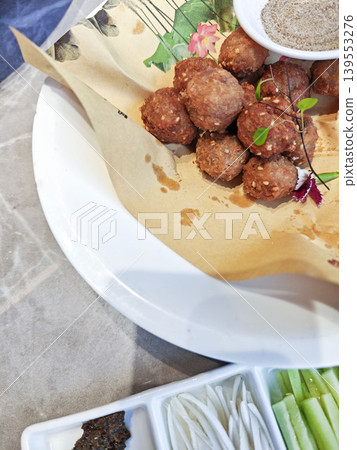 Plate of fried meatballs garnished with herbs and served with a small bowl of seasoning on a decorative paper, accompanied by sliced vegetables on a separate dish Plate of fried meatballs garnished with herbs and served with a small bowl of seasoning on a decorative paper, accompanied by sliced vegetables on a separate dish 139553276
