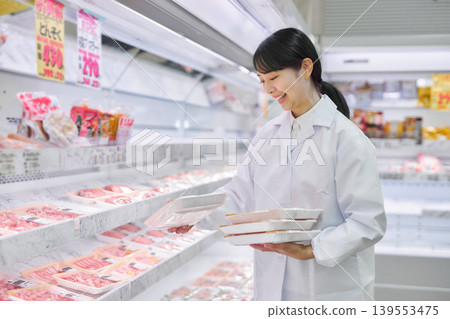 一位身穿白大褂的年輕女子正在超市整理肉類。 139553475