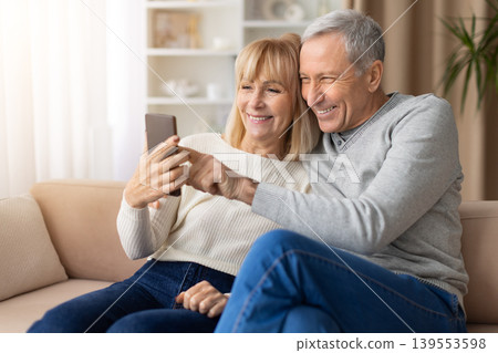 Smiling mature couple using smartphone together at home, enjoying digital communication Smiling mature couple using smartphone together at home, enjoying digital communication 139553598