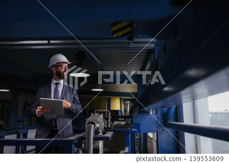 Engineer in hard hat supervising factory operations with digital tablet. Engineer in hard hat supervising factory operations with digital tablet. 139553609