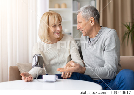 Smiling mature couple discussing health results after blood pressure check at home Smiling mature couple discussing health results after blood pressure check at home 139553617