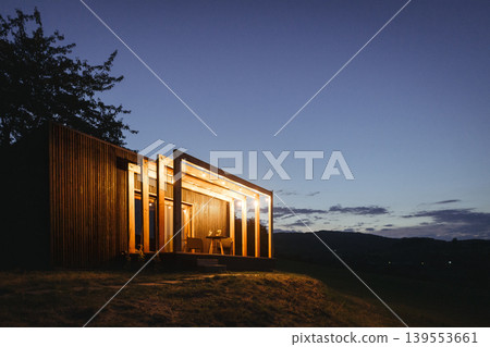 Stylish tiny home exterior at blue hour with warm ambient lighting. Stylish tiny home exterior at blue hour with warm ambient lighting. 139553661