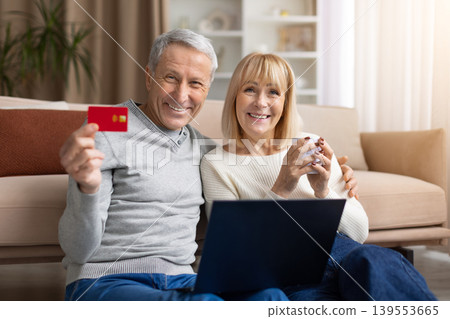 Senior couple showing credit card while sitting with laptop at home Senior couple showing credit card while sitting with laptop at home 139553665