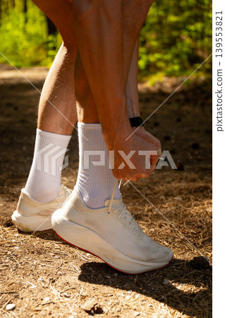 Close-up of a male runner tying the lace of his white sneaker Close-up of a male runner tying the lace of his white sneaker 139553821