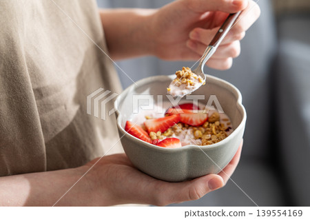 Healthy breakfast with yogurt, granola and fresh strawberries in a bowl, close-up hands Healthy breakfast with yogurt, granola and fresh strawberries in a bowl, close-up hands 139554169