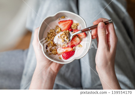 Healthy breakfast with yogurt, granola and fresh strawberries in a bowl, close-up hands 139554170