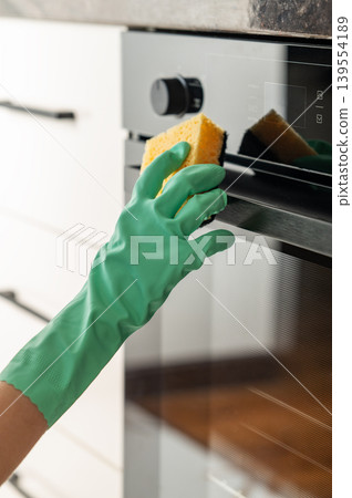 Cleaning the oven door with a sponge and a rubber glove, removing grease in a modern kitchen. 139554189