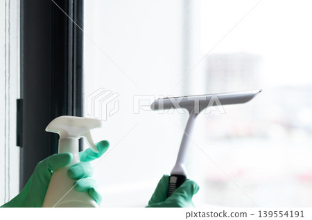 Washing the window with a gloved scraper and a spray bottle of detergent, removing water droplets Washing the window with a gloved scraper and a spray bottle of detergent, removing water droplets 139554191