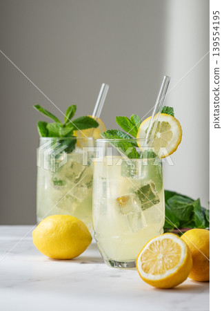 A refreshing summer drink with lemon, mint, and ice in a two glasses on a light background. 139554195