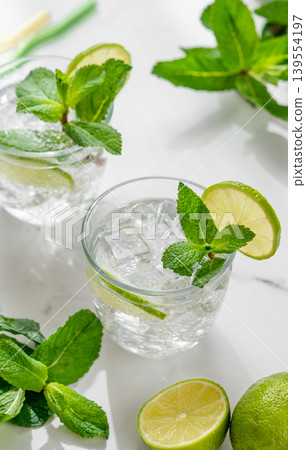 A fresh mojito with lime, mint and ice in glasses. Citrus lemonade or cocktail on a marble table A fresh mojito with lime, mint and ice in glasses. Citrus lemonade or cocktail on a marble table 139554197
