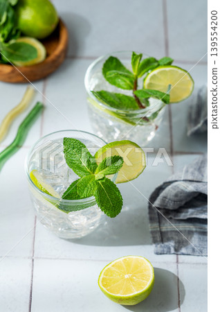 A fresh mojito with lime, mint and ice in glasses. Citrus lemonade or cocktail on a tile background A fresh mojito with lime, mint and ice in glasses. Citrus lemonade or cocktail on a tile background 139554200