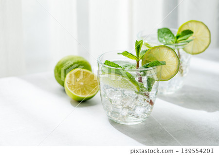 A fresh mojito with lime, mint and ice in glasses. Citrus lemonade or cocktail on a concrete table A fresh mojito with lime, mint and ice in glasses. Citrus lemonade or cocktail on a concrete table 139554201