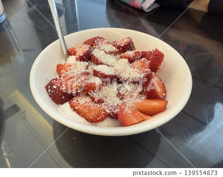 Bowl of fresh strawberries with shredded coconut on a reflective surface with a spoon Bowl of fresh strawberries with shredded coconut on a reflective surface with a spoon 139554873