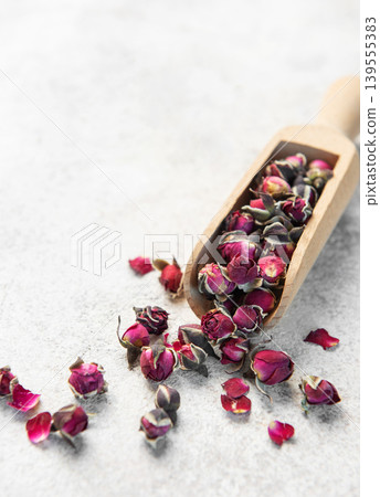 Dried rose buds spilling from wooden scoop 139555383