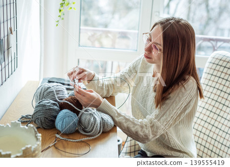 Woman knitting wool yarn at home for hobby Woman knitting wool yarn at home for hobby 139555419