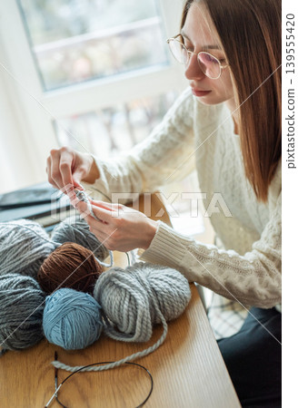 Woman knitting with yarn by window at home Woman knitting with yarn by window at home 139555420