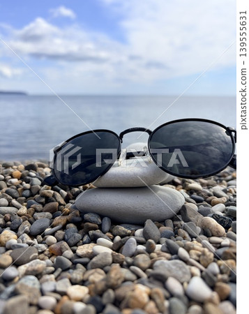 sunglasses with black round lenses lie on a smooth surface on the seashore sunglasses with black round lenses lie on a smooth surface on the seashore 139555631