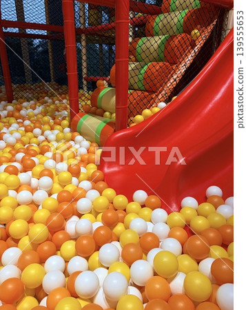 a vibrant section of an indoor soft-play area, focusing on a glossy red plastic slide that curves downward into a densely packed ball pit. a vibrant section of an indoor soft-play area, focusing on a glossy red plastic slide that curves downward into a densely packed ball pit. 139555653