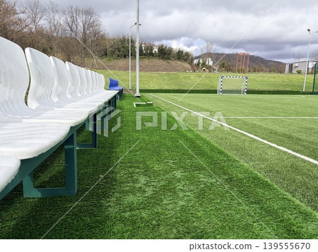 Empty white seats at mini soccer stadium. Outdoor soccer field with green artificial lawn. Empty white seats at mini soccer stadium. Outdoor soccer field with green artificial lawn. 139555670