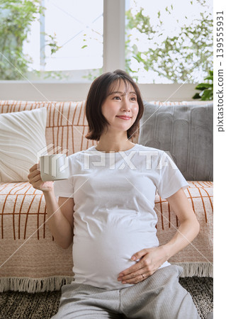 A smiling woman relaxing on a sofa, holding a coffee cup. 139555931