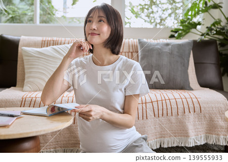 A pregnant woman sits on the living room sofa, reading a book and thinking. A pregnant woman sits on the living room sofa, reading a book and thinking. 139555933