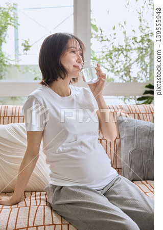 A woman sitting on a sofa and drinking water from a glass. 139555948