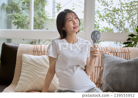 A pregnant woman cooling herself with a handheld fan. A pregnant woman cooling herself with a handheld fan. 139555952