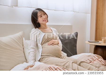 A pregnant woman smiles with her hand on her stomach while lying in bed. A pregnant woman smiles with her hand on her stomach while lying in bed. 139555955