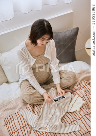 A pregnant woman and baby clothes look at an ultrasound image in bed. A pregnant woman and baby clothes look at an ultrasound image in bed. 139555968