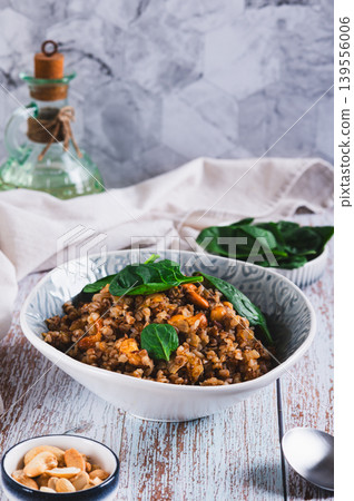 Vegetarian buckwheat with cashews and spinach in a bowl on the table vertical view Vegetarian buckwheat with cashews and spinach in a bowl on the table vertical view 139556006