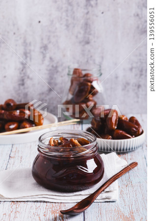 Sweet date marmalade in a jar and fruit in a bowl on a table vertical view 139556051