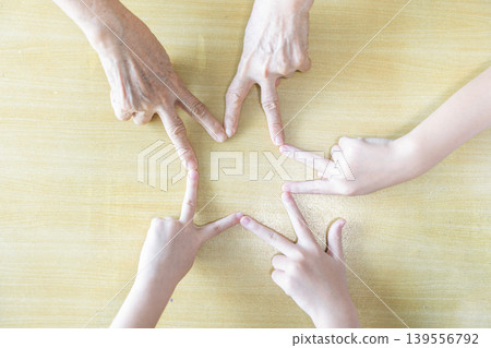 Children and an elderly woman point their fingers together to form a star, combining playful hand coordination with family unity and multigeneration teamwork. Children and an elderly woman point their fingers together to form a star, combining playful hand coordination with family unity and multigeneration teamwork. 139556792