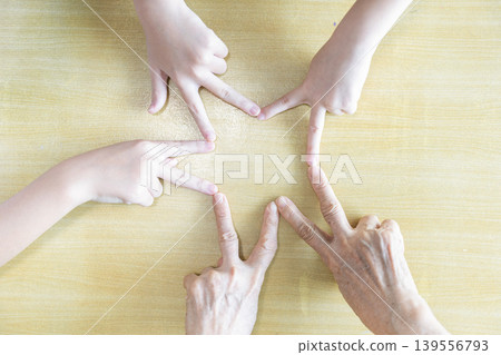 Children and an elderly woman point their fingers together to form a star, combining playful hand coordination with family unity and multigeneration teamwork. Children and an elderly woman point their fingers together to form a star, combining playful hand coordination with family unity and multigeneration teamwork. 139556793