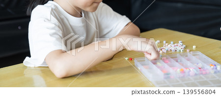 Small hands thread colorful beads onto elastic string, combining bracelet making with fine motor practice, finger control, and careful coordination development. Small hands thread colorful beads onto elastic string, combining bracelet making with fine motor practice, finger control, and careful coordination development. 139556804