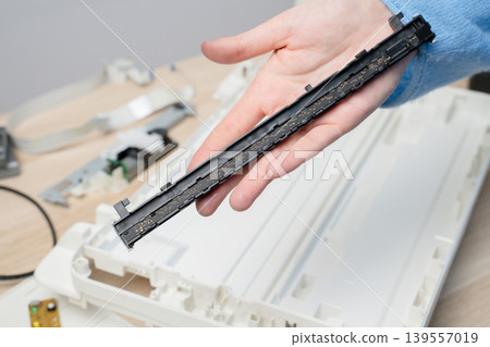 Close-up of a hand holding a disassembled flatbed scanner lighting component ,e performing scanner repair and maintenance on office equipment, showing electronic circuits and plastic casing details. 139557019