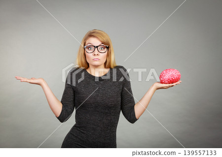Woman in eyeglasses being confused holding brain Woman in eyeglasses being confused holding brain 139557133