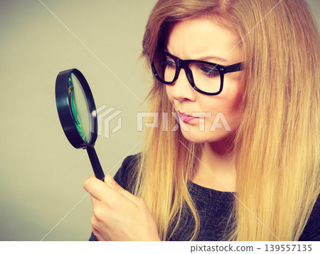 Woman holding magnifying glass investigating Woman holding magnifying glass investigating 139557135