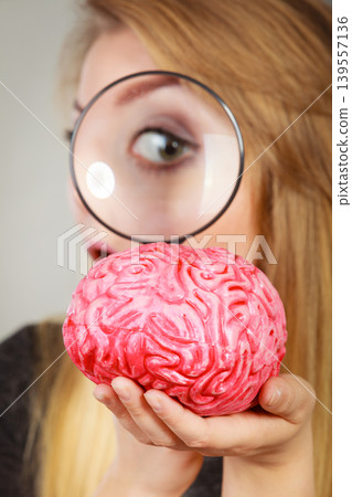 Woman holding magnifying glass investigating brain Woman holding magnifying glass investigating brain 139557136