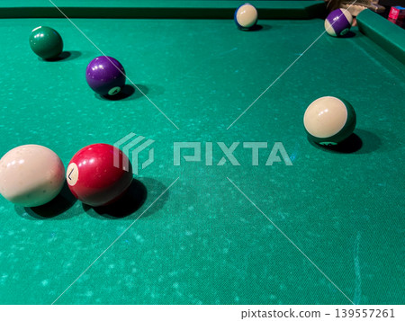 Colored balls are scattered on a green pool table in a recreation area as players enjoy a game at night Colored balls are scattered on a green pool table in a recreation area as players enjoy a game at night 139557261
