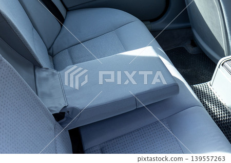 The backseat area of a car shows gray seats and a central armrest, possibly taken while parked or moving. Sunlight shines on the fabric The backseat area of a car shows gray seats and a central armrest, possibly taken while parked or moving. Sunlight shines on the fabric 139557263